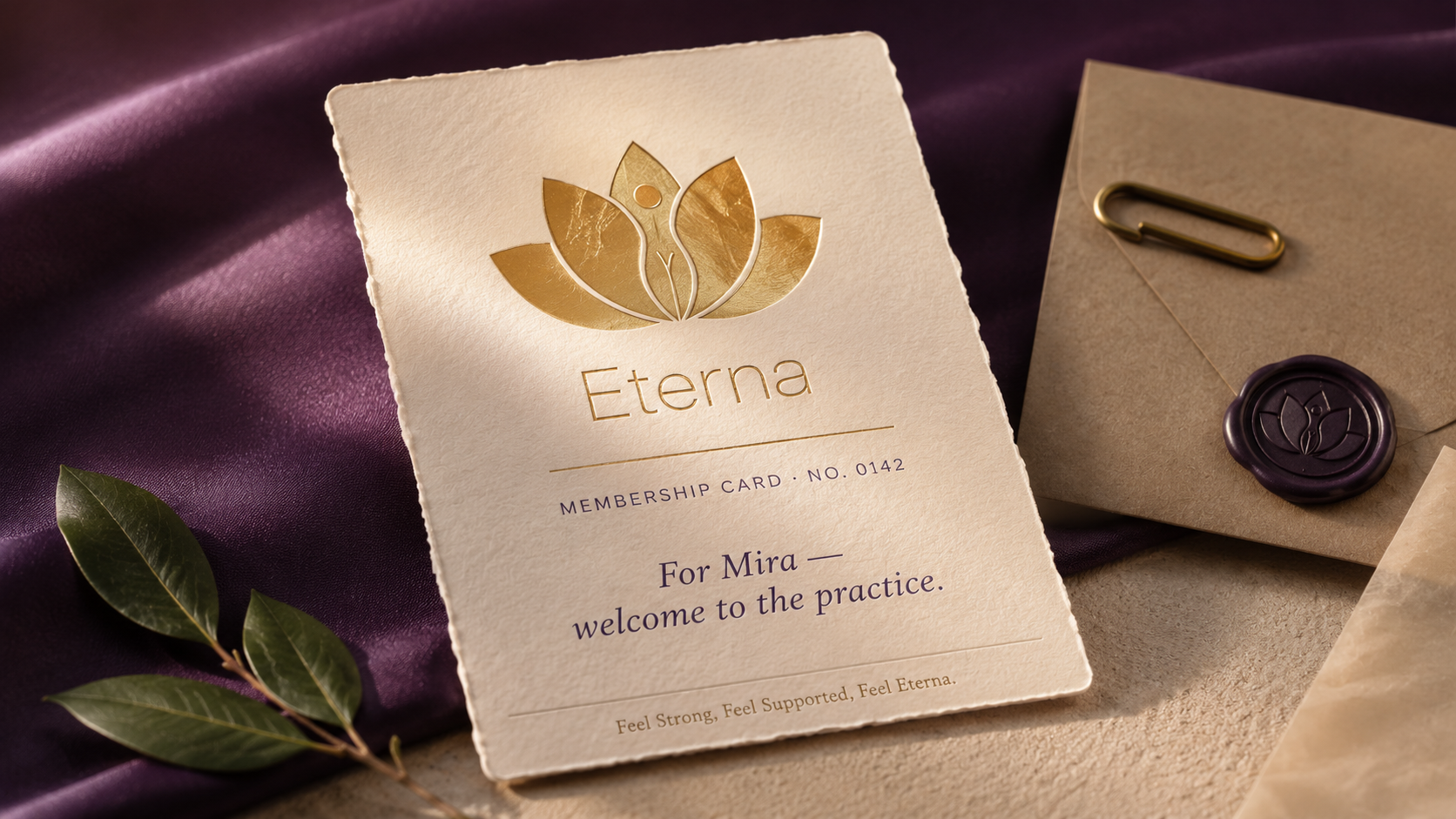 ETERNA membership welcome card macro hero — cream deckled-edge cotton card with the lotus+figure mark and Eterna wordmark in antique-brass hot-foil emboss, Membership Card · No. 0142 in small caps, For Mira welcome to the practice in elegant serif italic, Feel Strong Feel Supported Feel Eterna tagline, dusty-plum silk under-surface, kraft envelope with deep-purple wax seal of the lotus mark, bay laurel leaf